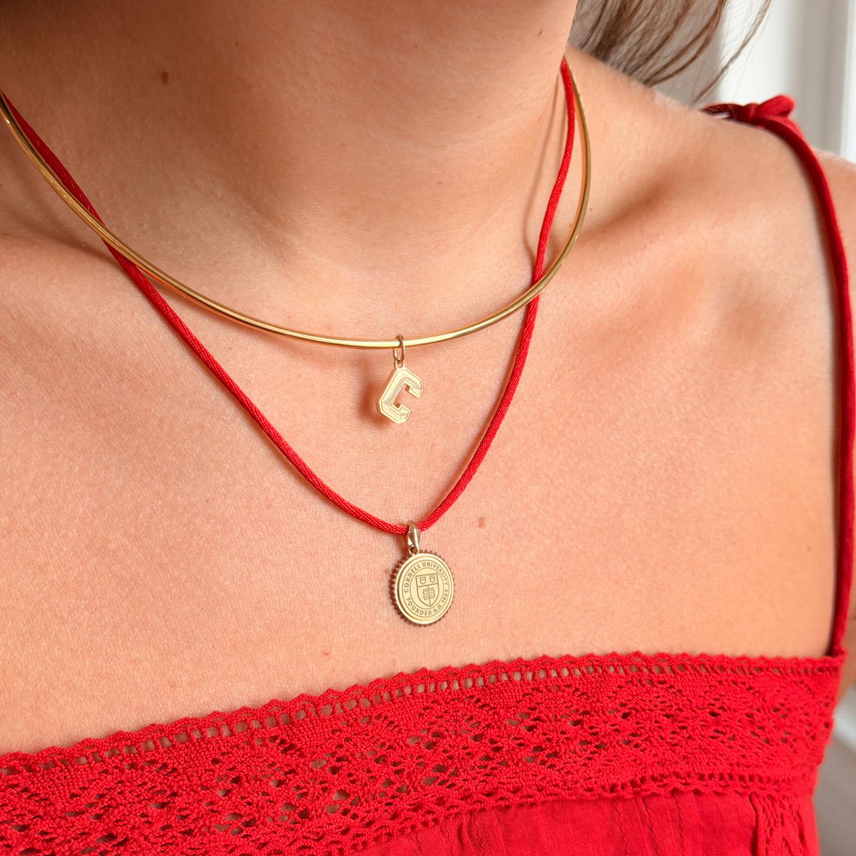 A close-up of a person wearing a double-strand necklace set. The top layer is a thin gold-tone metal chain with a small gold initial 'C' pendant.