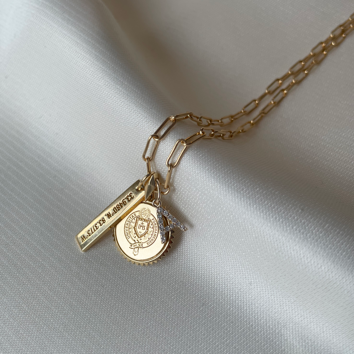 Fordham Sunburst Charm shown with the Coordinates Bar and Diamond Letter A on Link Chain in gold laydown