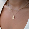 Close-up of a person wearing a gold necklace with a tag pendant on a white background
