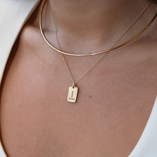 Close-up of a person wearing a gold necklace with a tag pendant on a white background