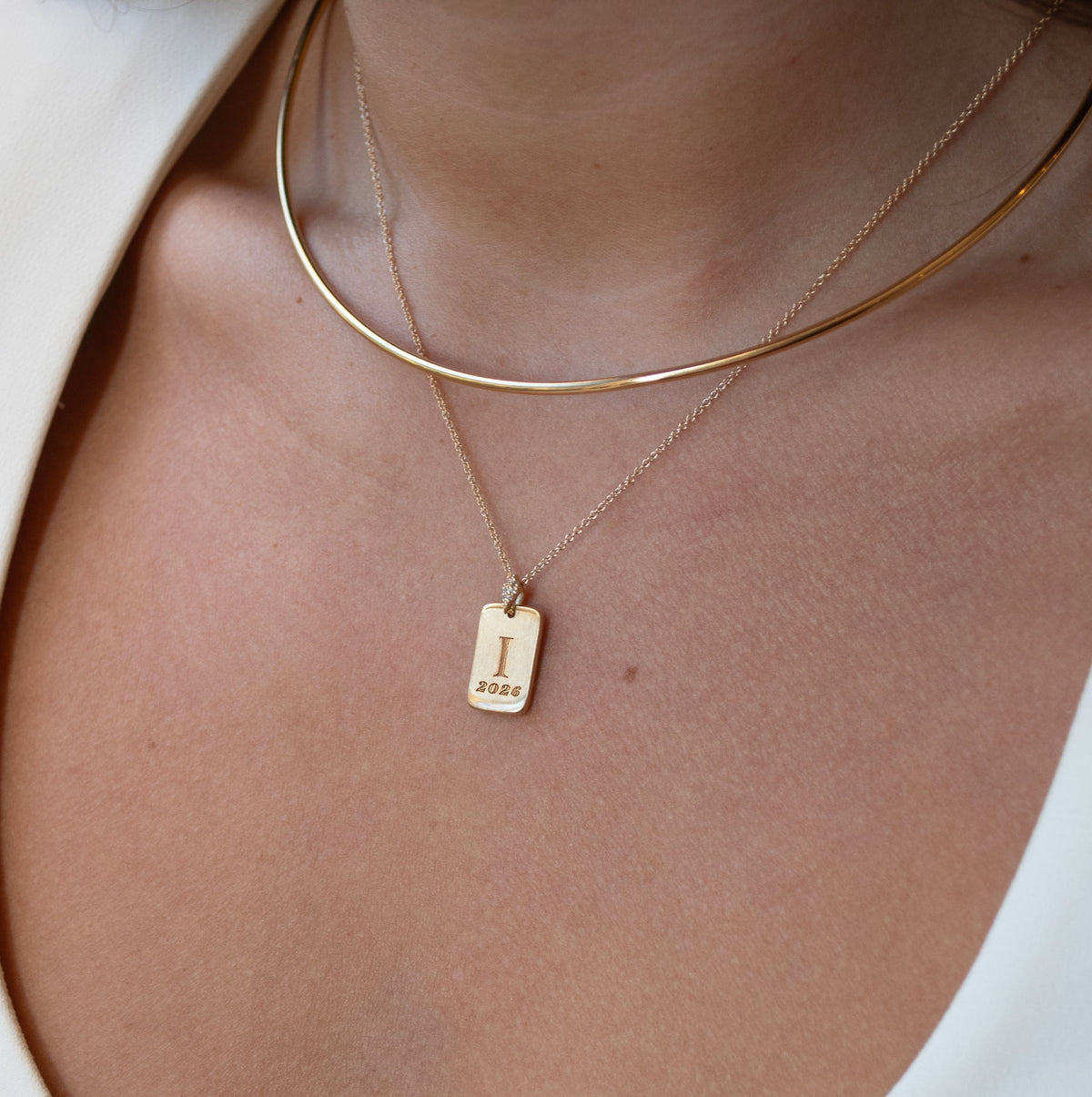 Close-up of a person wearing a gold necklace with a tag pendant on a white background