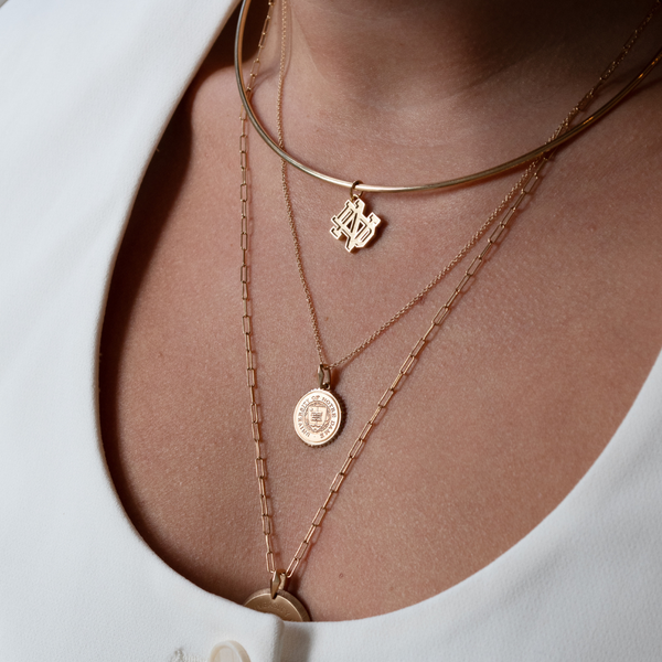 Notre Dame Logo Charm shown on figure in gold on Neck Collar with Notre Dame Sunburst Pendant on Cable Chain