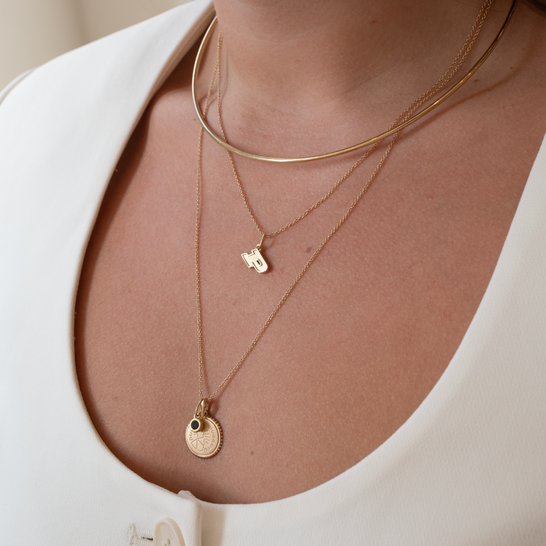 Purdue Logo Charm shown on figure in gold on Cable Chain with Purdue Sunburst and Black Onyx Gemstone in gold on long Cable Chain with Neck Collar in gold