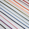 A close-up of multiple thin cords or threads arranged diagonally on a white background, shown in several colors including black, purple, pink, blue, green, orange, and red.