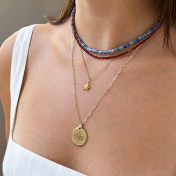 Close-up of a person wearing multiple necklaces with a focus on a gold coin pendant.