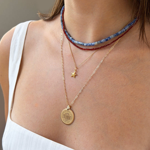 Close-up of a person wearing multiple necklaces with a focus on a gold coin pendant.