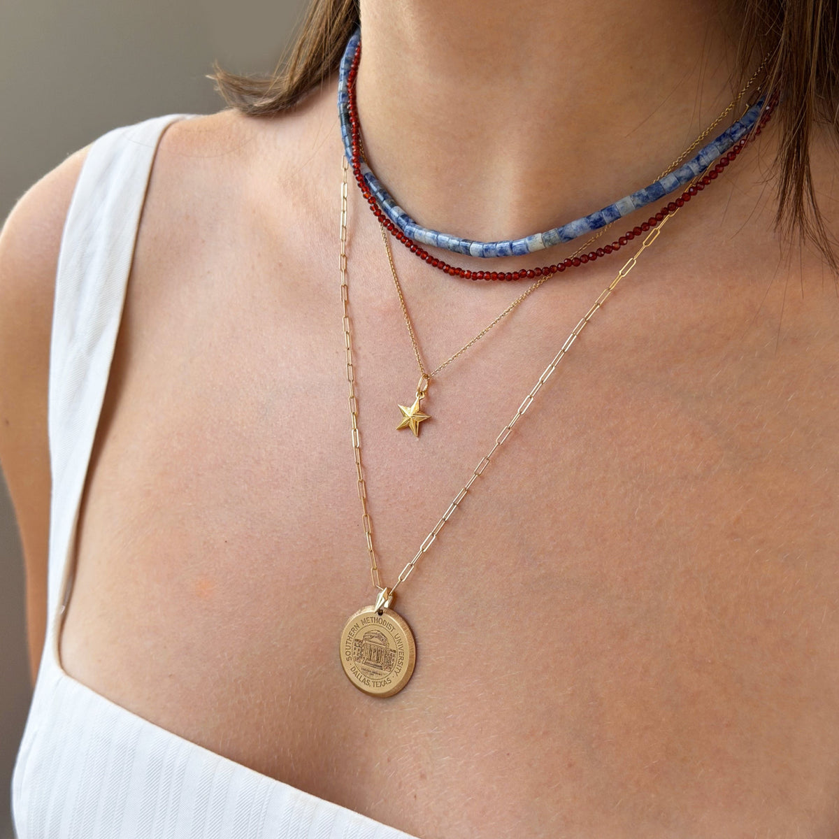 Close-up of a person wearing multiple necklaces with a focus on a gold coin pendant.