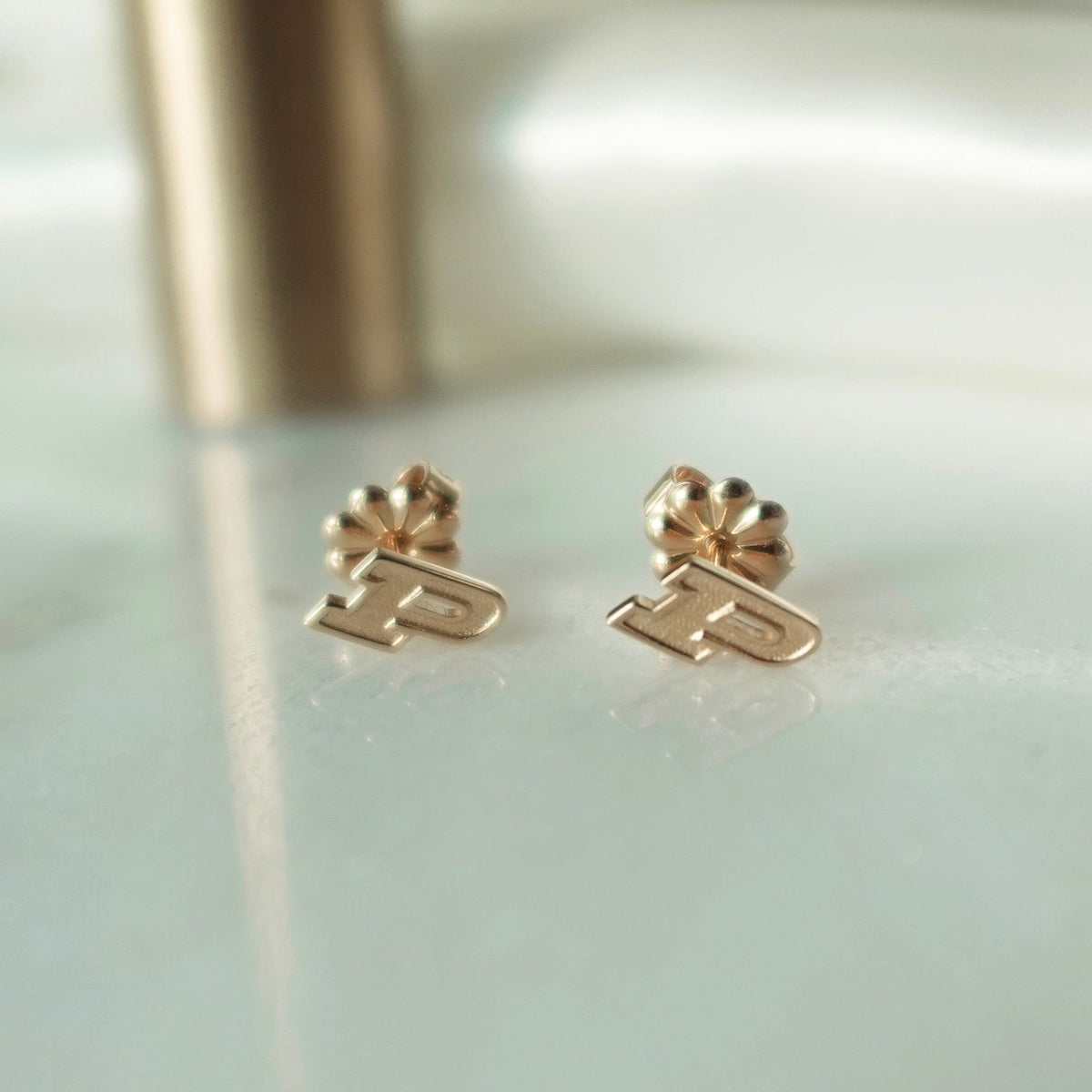 Purdue P Stud Earrings shown in gold laydown